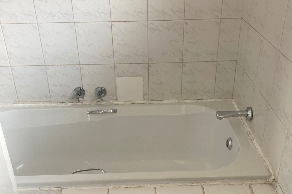 A dated bathroom featuring a built-in bathtub with wall-mounted fixtures and tiled surround, requiring maintenance and cosmetic updates.