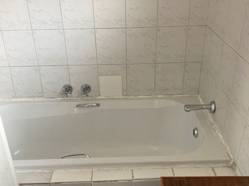 A dated bathroom featuring a built-in bathtub with wall-mounted fixtures and tiled surround, requiring maintenance and cosmetic updates.