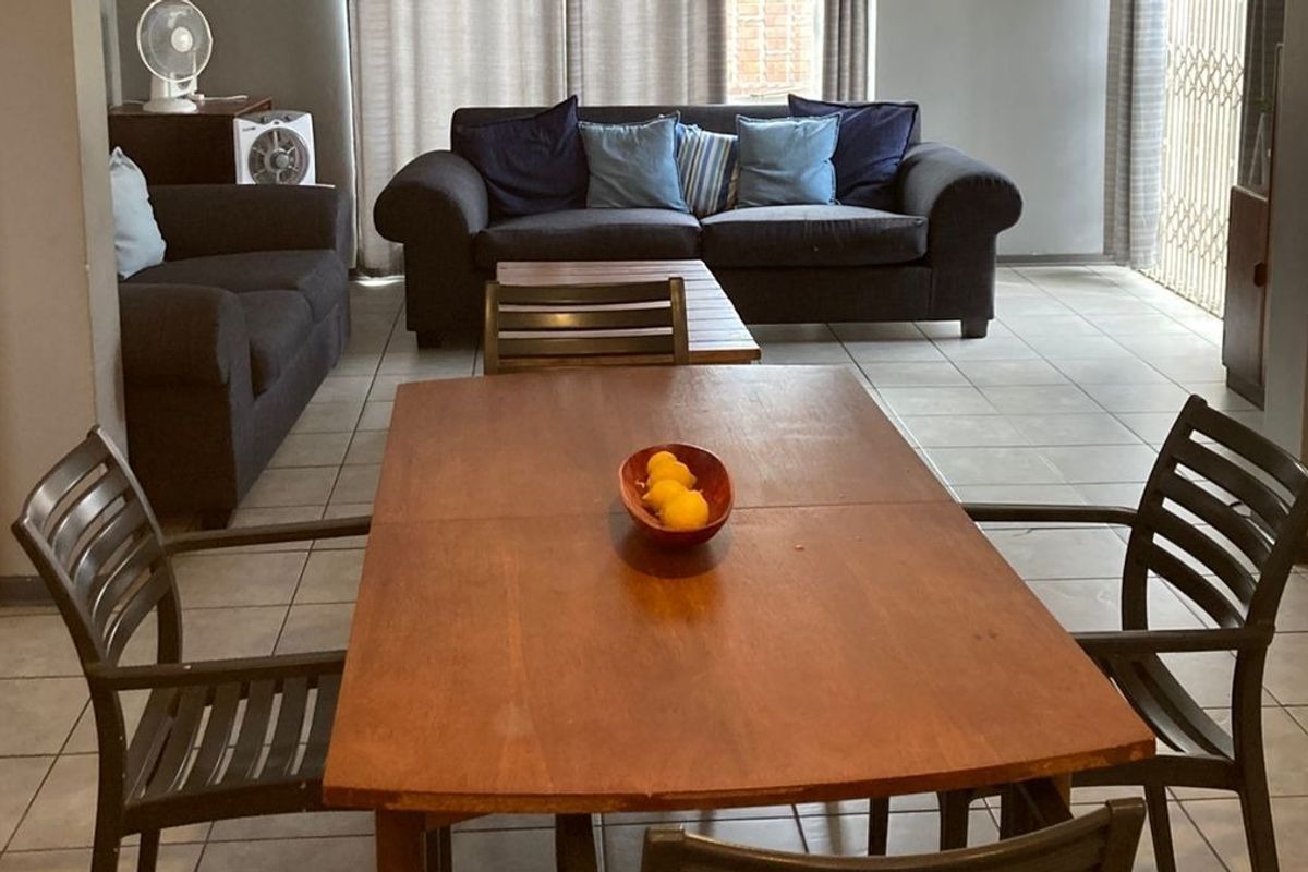 An open-plan living and dining area featuring neutral tiled flooring and access to an outdoor space through a sliding glass door.
