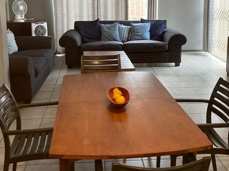 An open-plan living and dining area featuring neutral tiled flooring and access to an outdoor space through a sliding glass door.