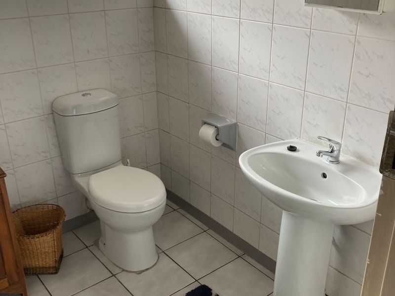 A functional guest bathroom featuring a pedestal basin, toilet, and neutral wall tiling with security bars on the window.