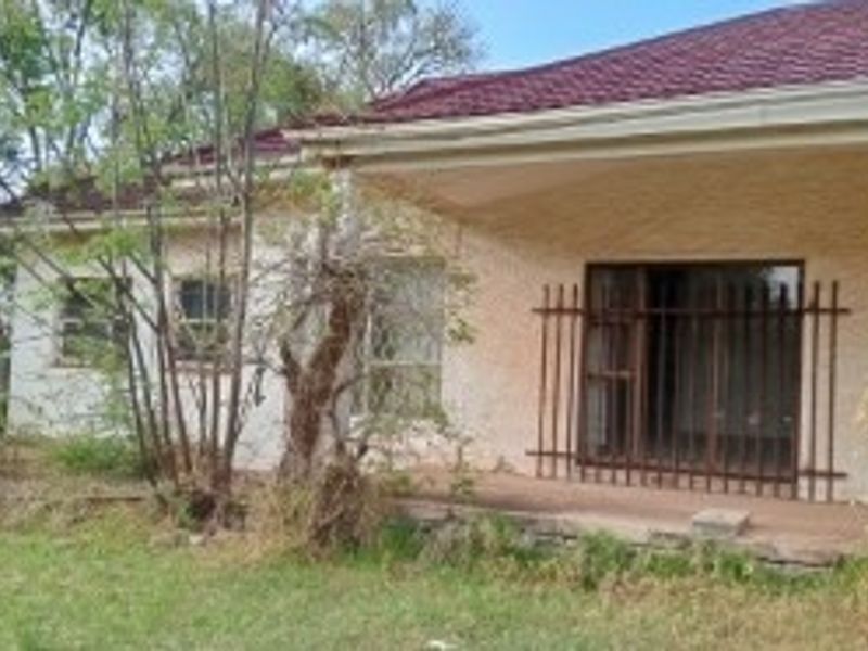 Rear exterior view of the house featuring a covered patio, sliding glass doors with security bars, and a tiled roof, requiring significant landscaping and maintenance.