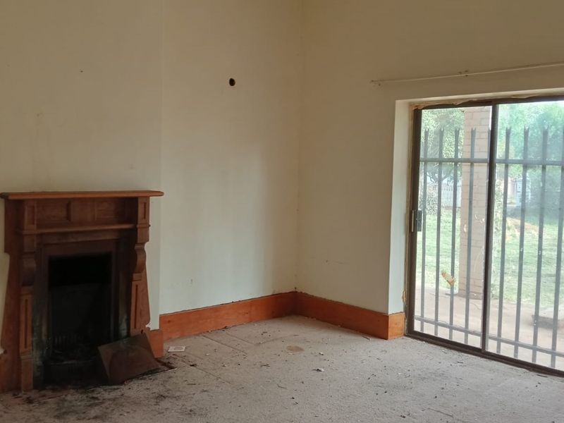 An empty living room featuring a traditional wooden fireplace mantel and a sliding glass door with security bars leading to the garden.