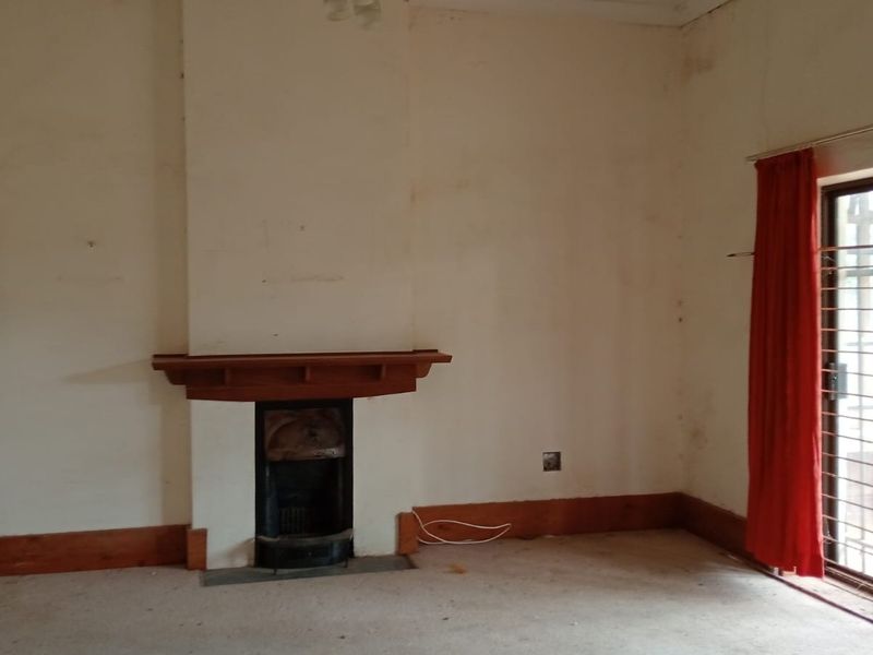 An empty living room featuring a traditional fireplace with a wooden mantelpiece, sliding glass doors with security gates, and worn carpeting.