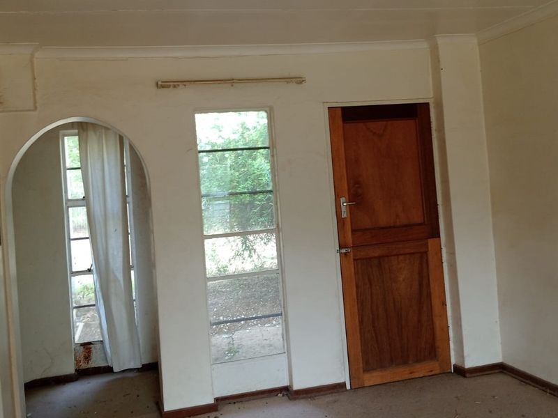 An empty living area featuring an arched doorway, timber stable door, and steel-framed windows, requiring cosmetic updates and maintenance to restore its appeal.