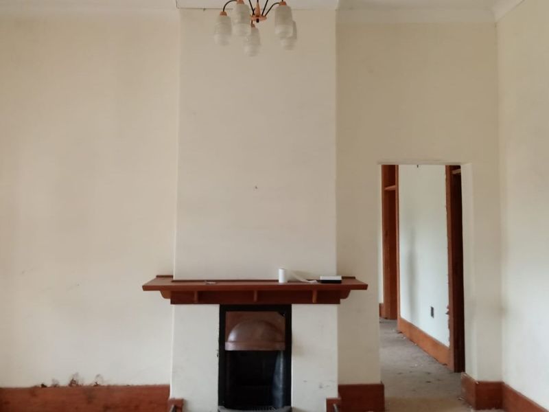 An empty living room featuring a central fireplace with a wooden mantelpiece, requiring cosmetic updates to the walls and finishes.