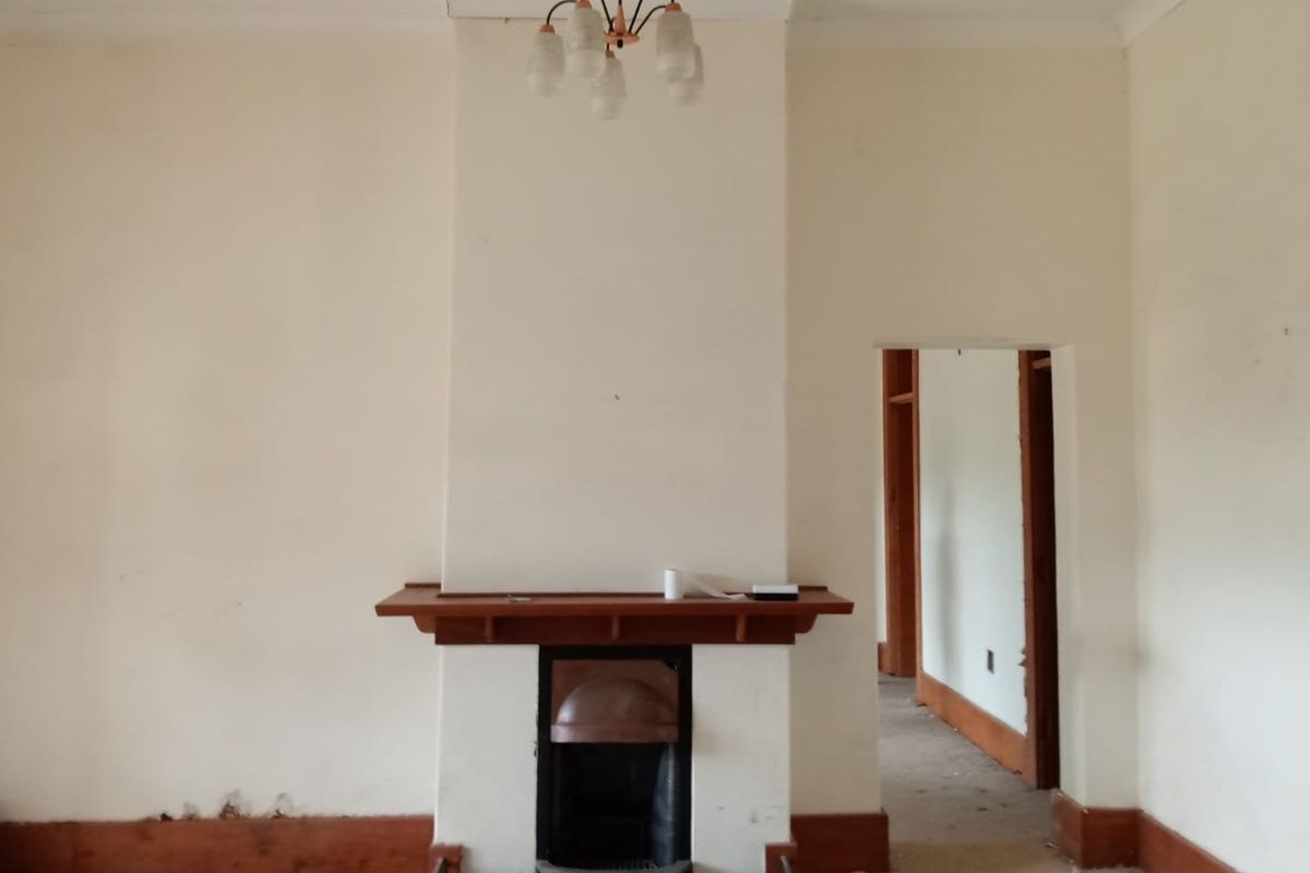 An empty living room featuring a central fireplace with a wooden mantelpiece, requiring cosmetic updates to the walls and finishes.