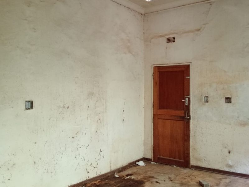 An empty bedroom space requiring significant renovation, featuring worn wall finishes, a timber door, and built-in cupboard storage.