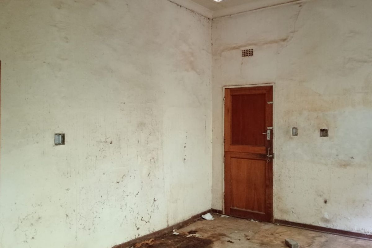 An empty bedroom space requiring significant renovation, featuring worn wall finishes, a timber door, and built-in cupboard storage.
