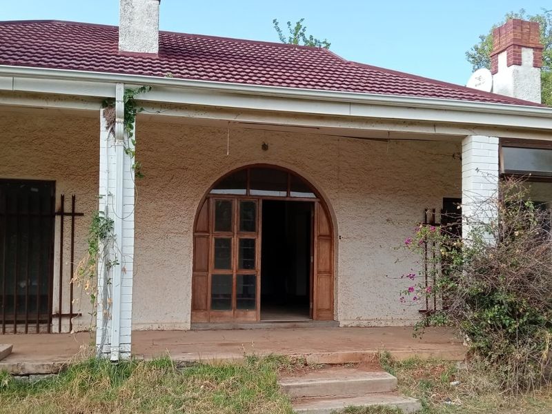 Front elevation of a house featuring a covered patio, arched wooden entrance door, and tiled roof, requiring exterior maintenance and landscaping.