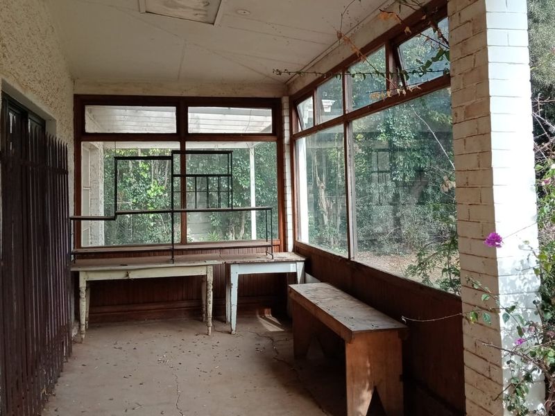An enclosed patio area featuring large glass windows, a concrete floor, and a brick pillar, offering potential for a bright sunroom or outdoor living space.