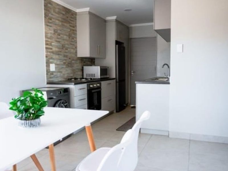 Modern open-plan kitchen featuring stone veneer backsplash, built-in cabinetry, integrated appliances, and tiled flooring, seamlessly flowing into the dining area.