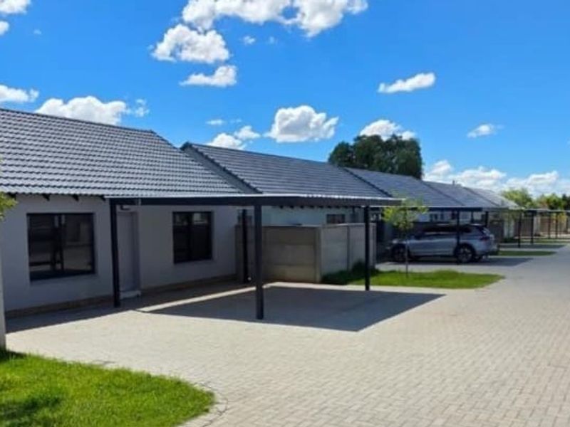 Front exterior view of a townhouse complex featuring paved driveways, individual carports, and well-maintained tiled roof structures.