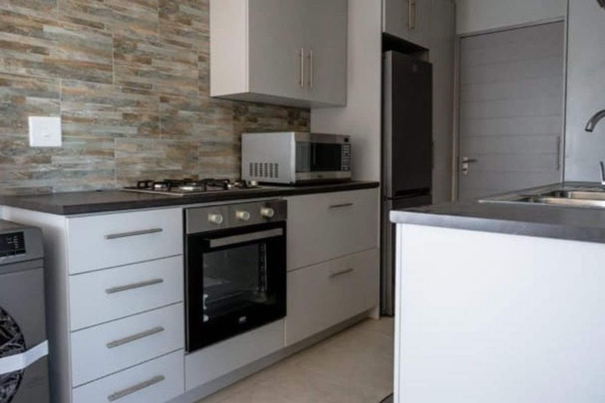 Modern kitchen featuring sleek grey cabinetry, stone-look tile splashback, built-in oven, gas hob, and integrated sink with contemporary finishes.