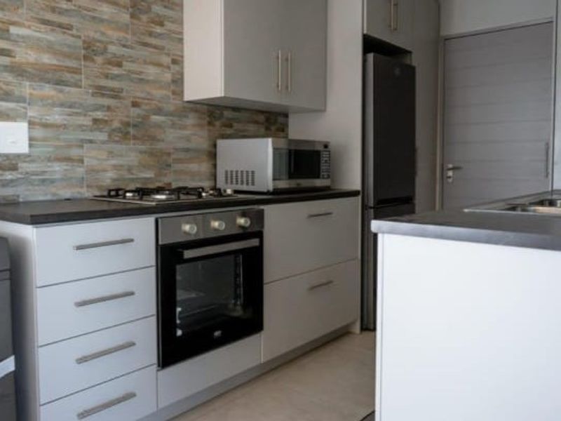 Modern kitchen featuring sleek grey cabinetry, stone-look tile splashback, built-in oven, gas hob, and integrated sink with contemporary finishes.