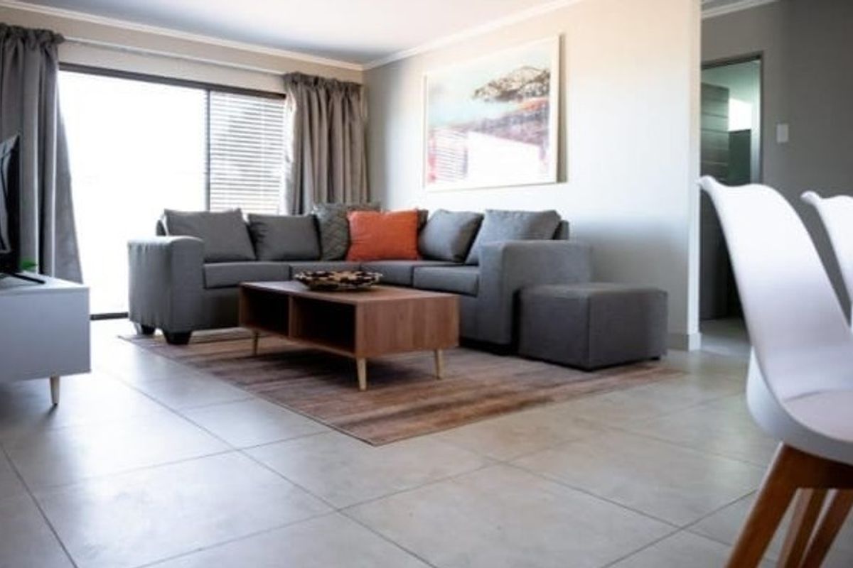 A bright open-plan living area featuring large format floor tiles, neutral wall finishes, and a sliding glass door providing access to the exterior.