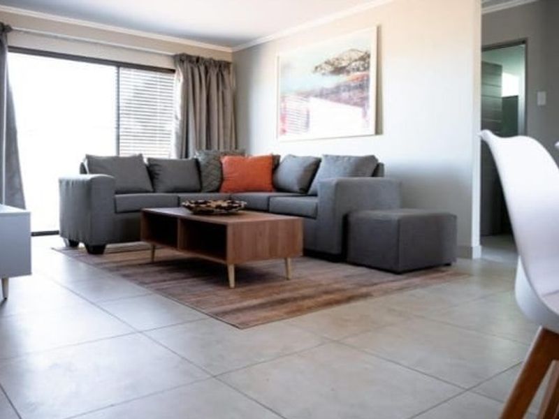 A bright open-plan living area featuring large format floor tiles, neutral wall finishes, and a sliding glass door providing access to the exterior.