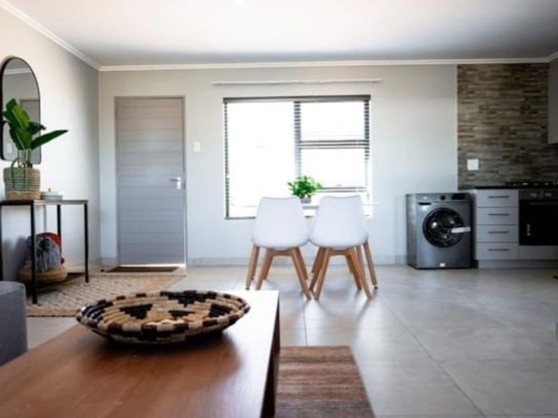 An open-plan living and kitchen area featuring tiled floors, a stone feature wall, and modern built-in kitchen cabinetry with integrated appliances.