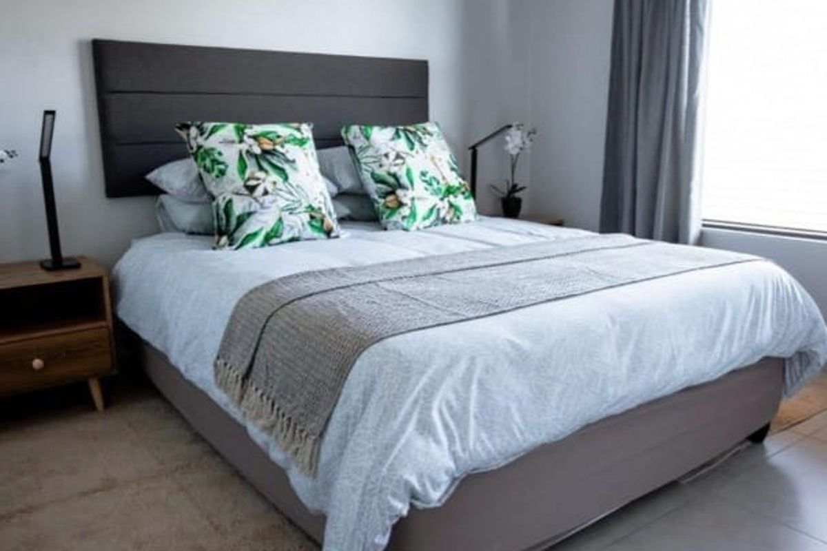 A well-maintained bedroom featuring neutral wall finishes, tiled flooring, and a large window with fitted blinds for natural light.