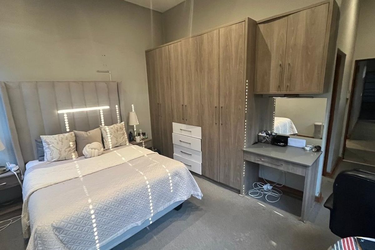A well-maintained bedroom featuring extensive built-in wooden cabinetry with an integrated vanity station and neutral carpeting.