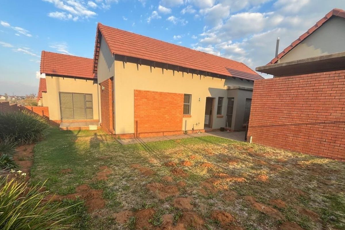 Rear view of the townhouse featuring a tiled roof, brick and plastered exterior walls, and a small private garden area with paved patio.