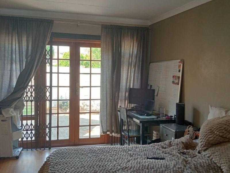 Bedroom featuring laminate flooring and wooden french doors with a security gate, providing direct access to the outdoor area.