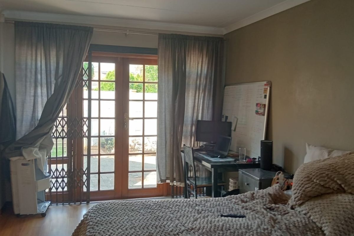 Bedroom featuring laminate flooring and wooden french doors with a security gate, providing direct access to the outdoor area.