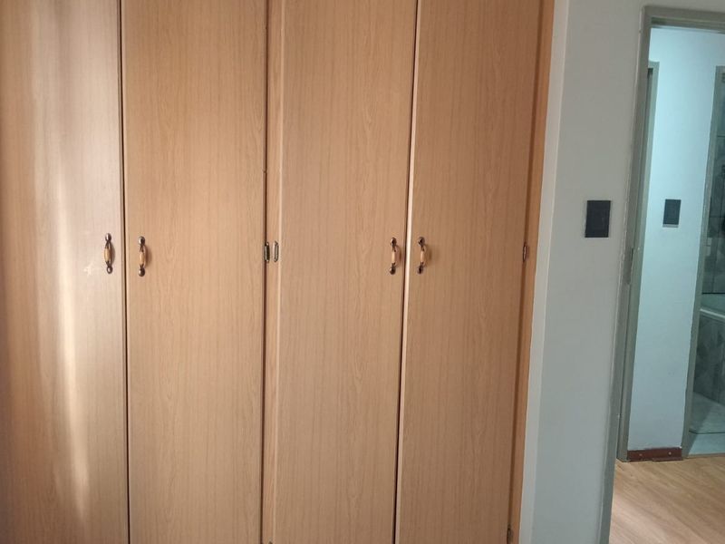 Bedroom featuring light wood-finish built-in cupboards and laminate flooring, with an adjacent view into a tiled bathroom.