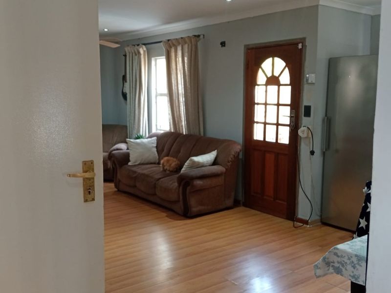 A living room featuring laminate flooring, coved cornicing, and a timber entrance door, viewed from an adjacent room.