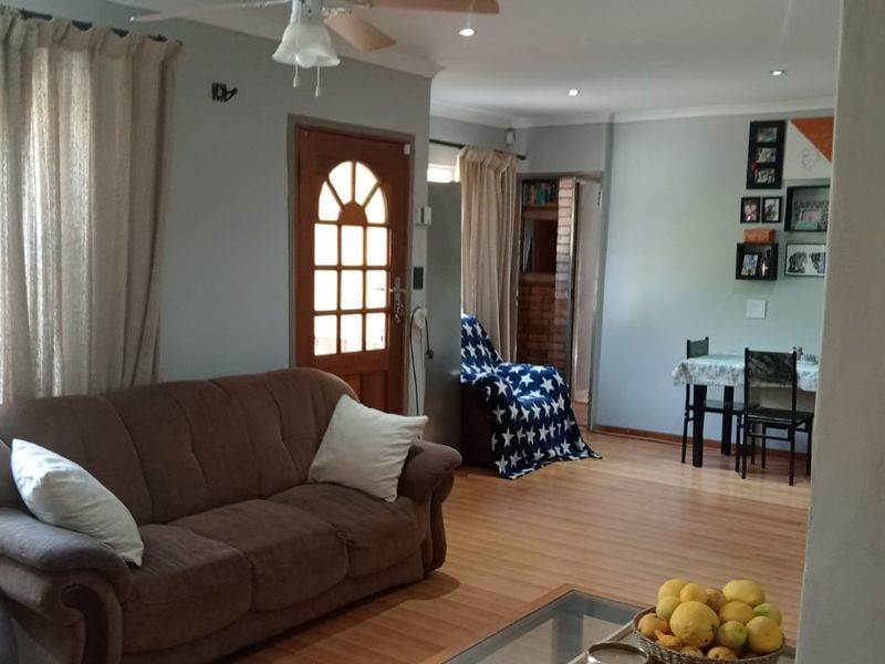 A living room featuring laminate flooring, a ceiling fan, and a timber entrance door, providing a functional and open living space.