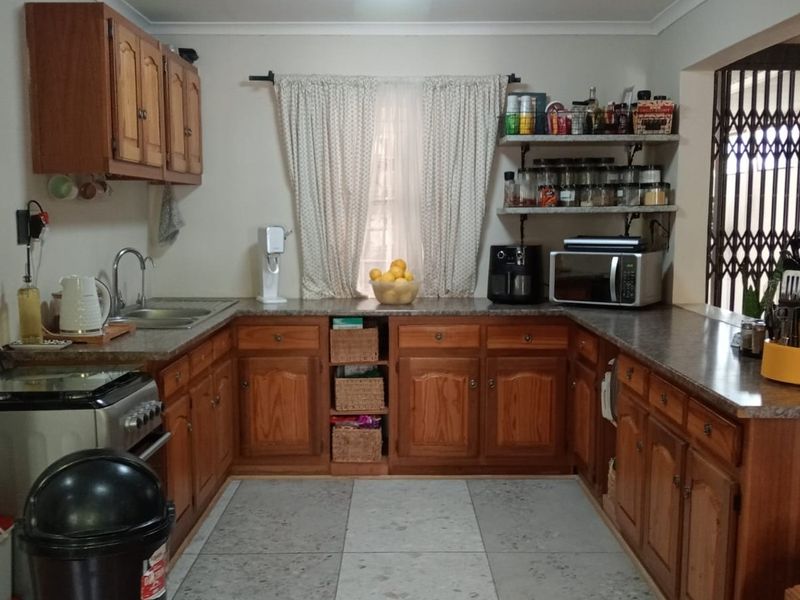 A functional kitchen featuring traditional wooden cabinetry, laminate countertops, open shelving, and tiled flooring, offering a classic layout with ample storage space.
