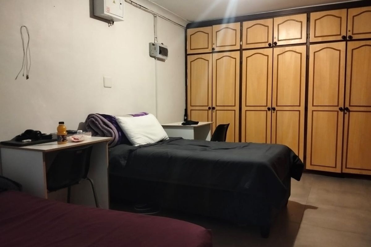 A bedroom featuring built-in wooden cupboards and tiled flooring, with visible electrical conduit and distribution board on the wall.