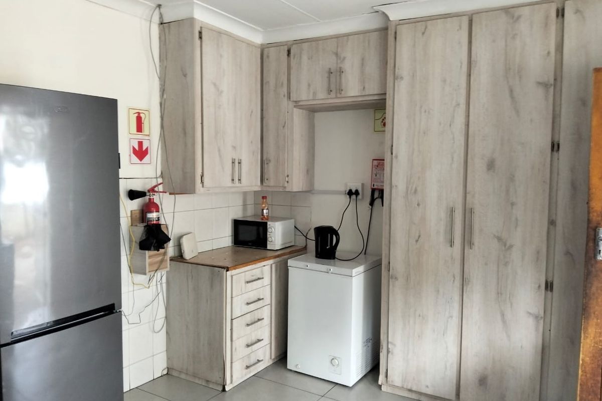 A functional kitchen area featuring light wood-look cabinetry, tiled backsplash, and ample storage space with a built-in pantry cupboard.