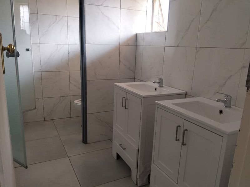 Modern bathroom featuring a double vanity with white cabinetry, floor-to-ceiling marble-look wall tiles, and a separate shower enclosure.