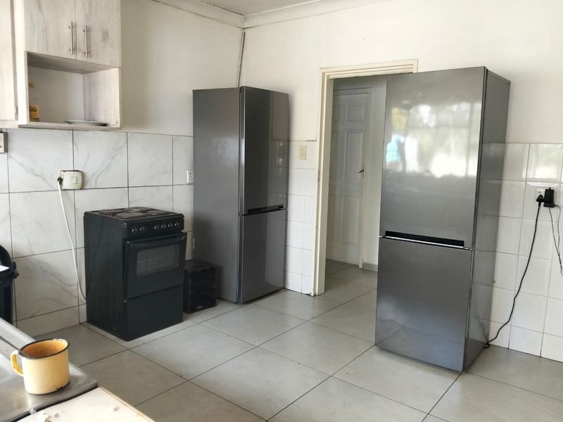 A functional kitchen area featuring tiled flooring, tiled splashbacks, and built-in cabinetry, requiring some maintenance to address exposed wiring and wall finishes.