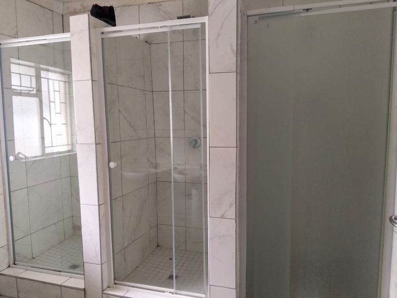A functional bathroom featuring multiple glass shower enclosures with tiled walls and flooring, providing a clean and practical layout.