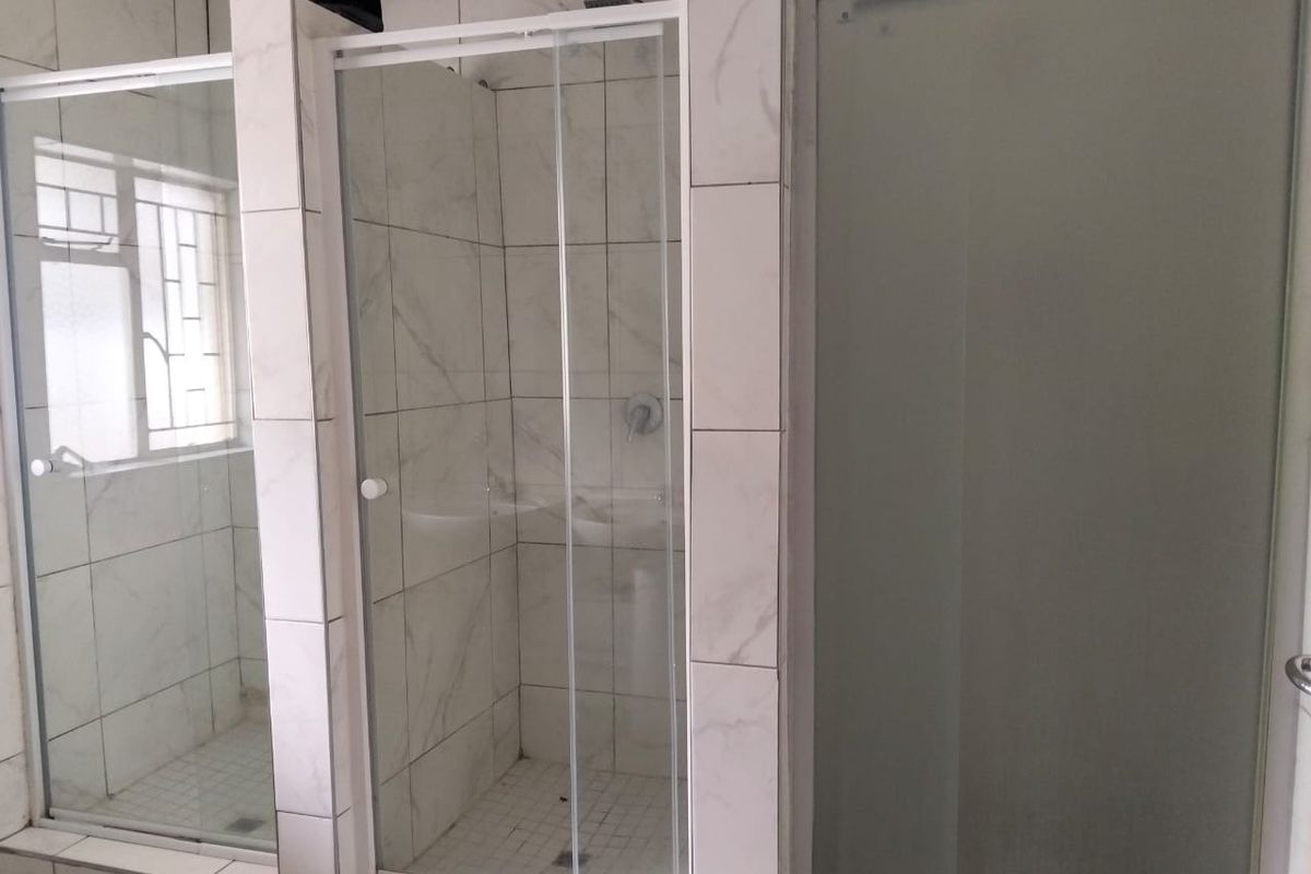 A functional bathroom featuring multiple glass shower enclosures with tiled walls and flooring, providing a clean and practical layout.