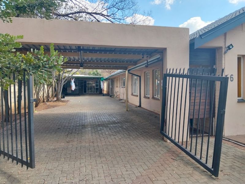 Front view of the property featuring a paved driveway, a covered carport, and a secure metal entrance gate.