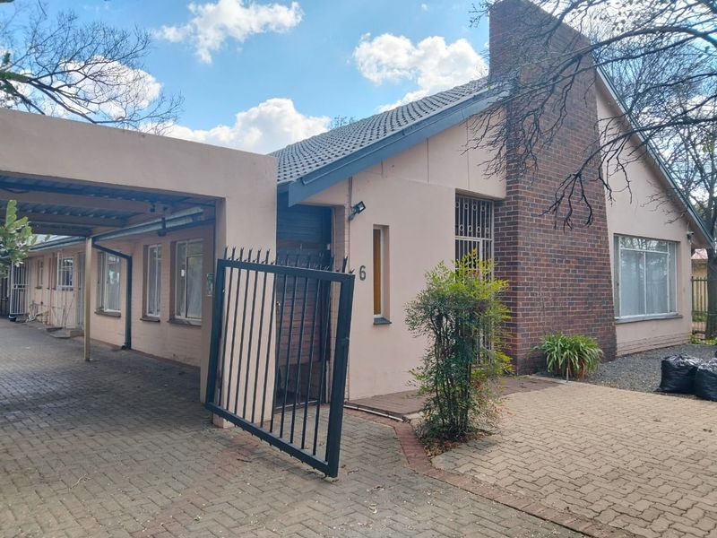 Front exterior view of a single-story house featuring a brick chimney, paved driveway, carport, and security gate.