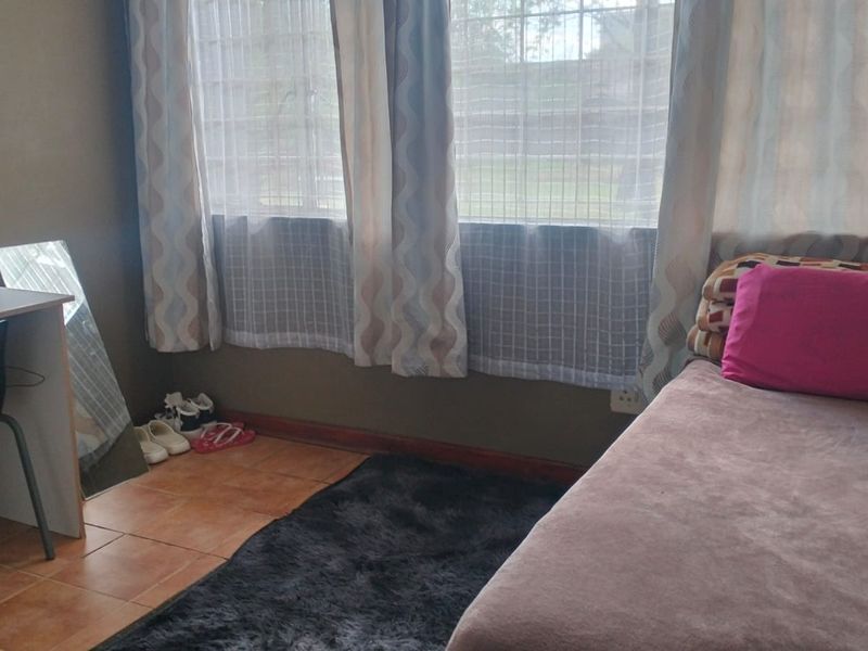 A bedroom featuring tiled flooring and windows fitted with security bars, providing a functional living space.