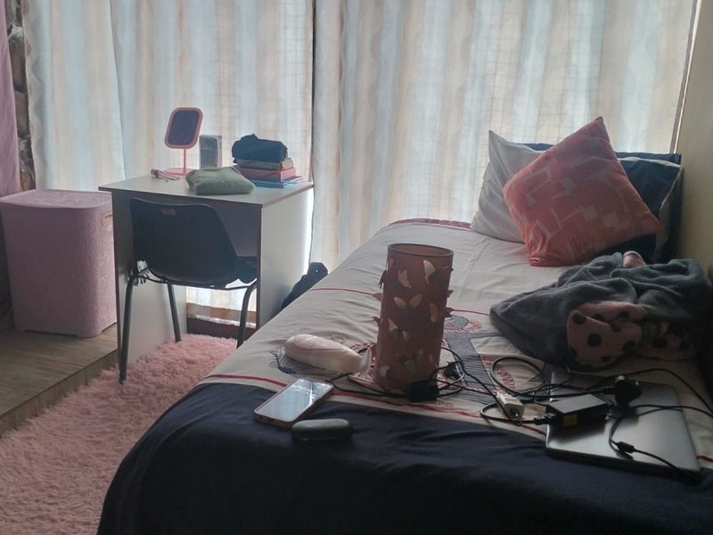 A bedroom featuring tiled flooring and natural light from a window covered by curtains.