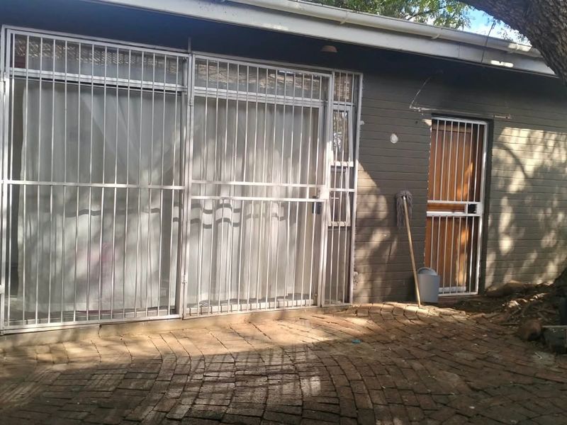 Rear exterior view of the property featuring brick paving, security gates, and a timber door, with mature tree landscaping.
