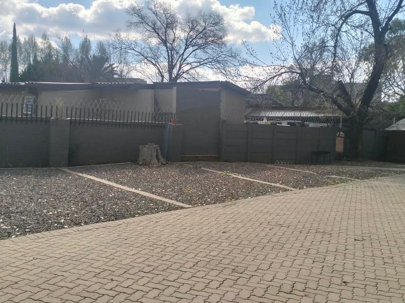 Front exterior view featuring a paved driveway, gravel parking bays, and a secure perimeter wall with security spikes.