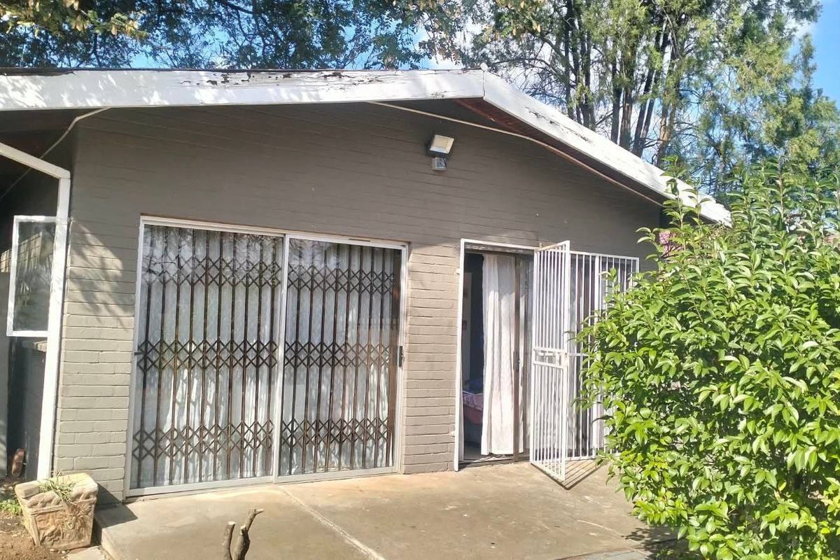 Rear exterior view of the house featuring a concrete patio, sliding glass doors with security gates, and visible wear on the roof fascia.