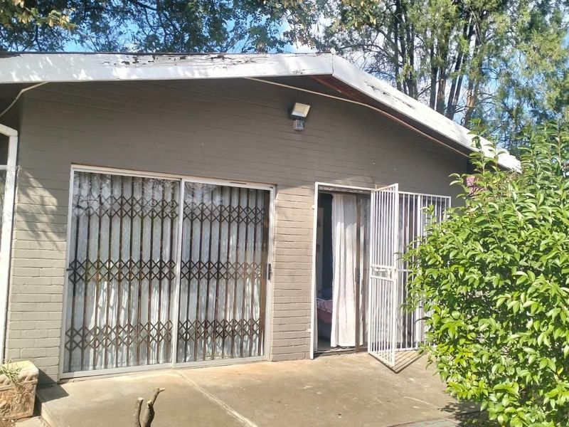 Rear exterior view of the house featuring a concrete patio, sliding glass doors with security gates, and visible wear on the roof fascia.