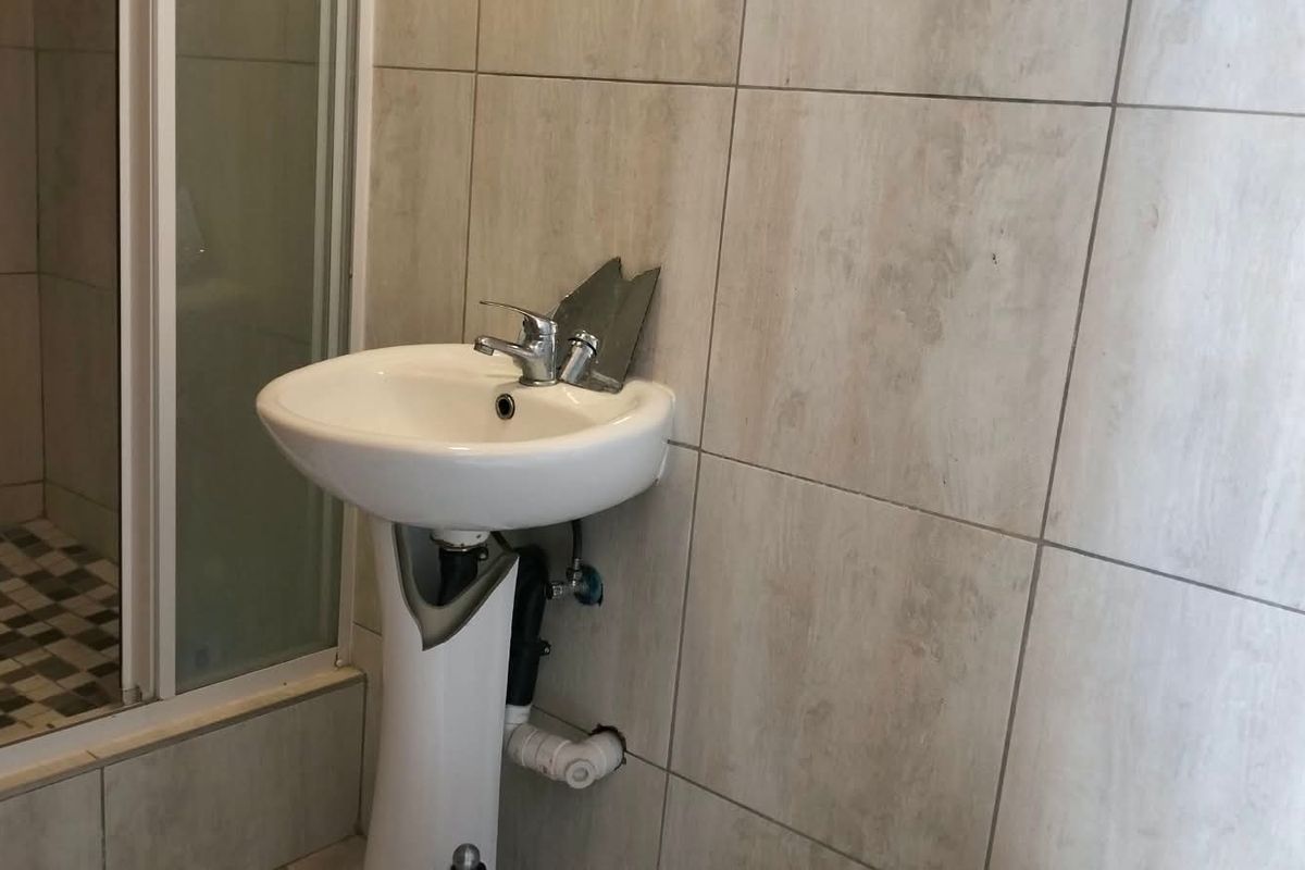 A functional bathroom featuring a pedestal basin and a shower enclosure with neutral wall tiling, requiring minor repairs to fixtures and finishes.