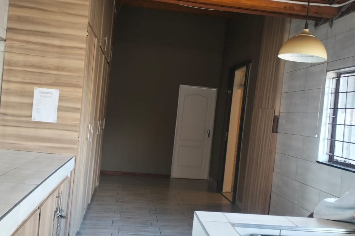 A spacious kitchen area featuring extensive built-in cabinetry, tiled countertops, and exposed timber ceiling beams, offering a functional layout ready for personalization.