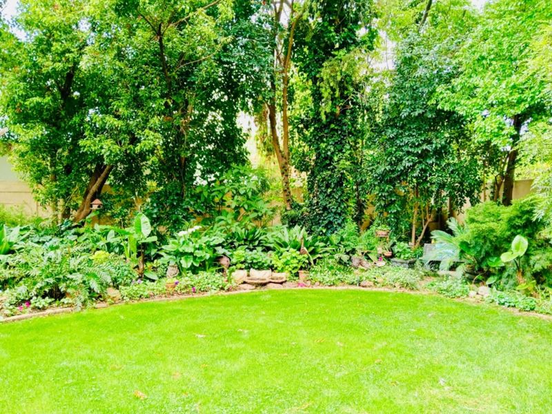 A lush, well-maintained private garden featuring a manicured lawn, mature trees, and established perimeter landscaping.