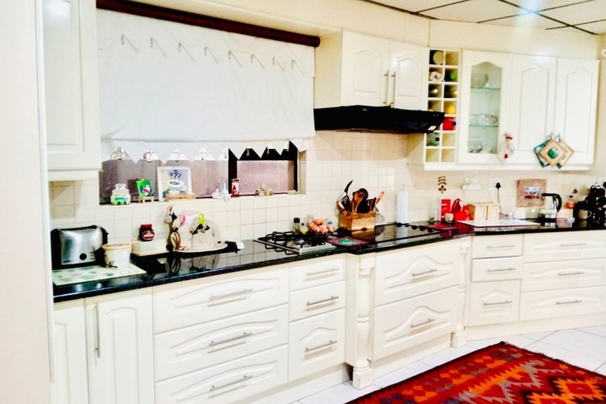 A functional kitchen featuring cream-colored cabinetry, granite countertops, a gas hob, and an integrated extractor fan with a tiled backsplash.