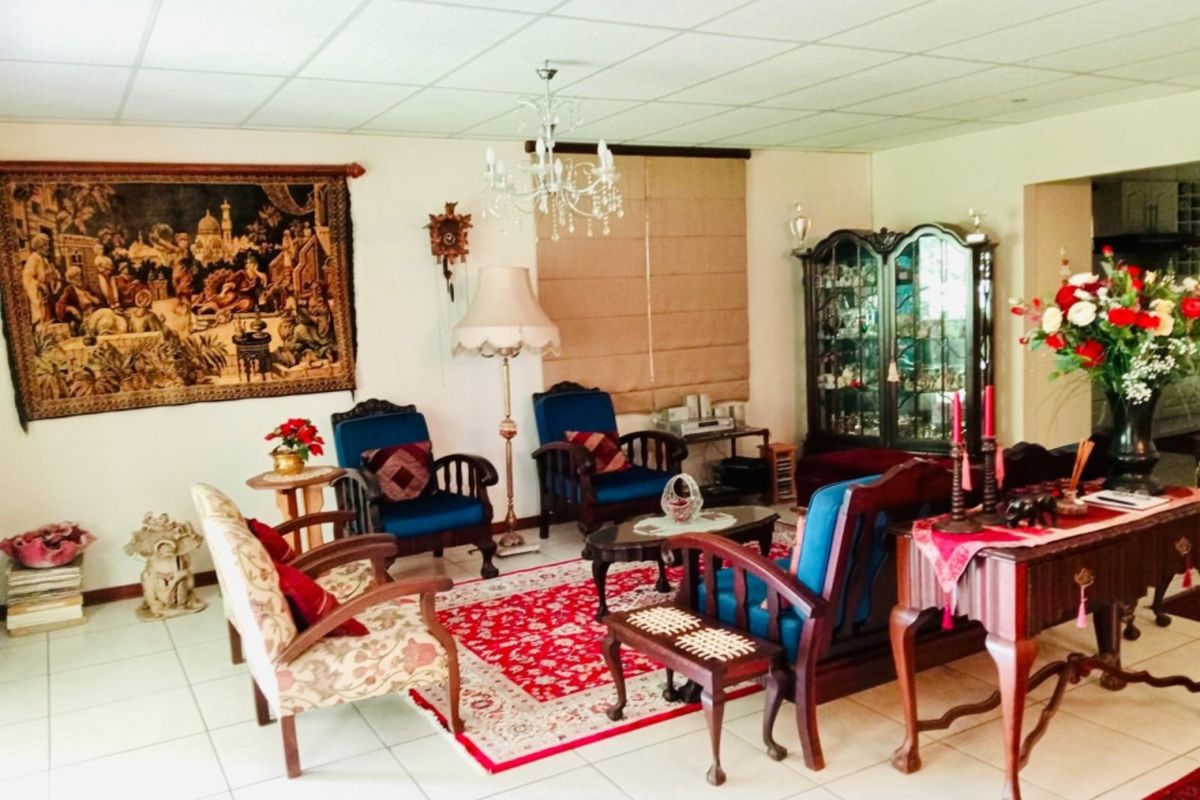 A spacious living room featuring tiled flooring, a drop ceiling, and a central chandelier, offering a traditional layout with ample space for seating.